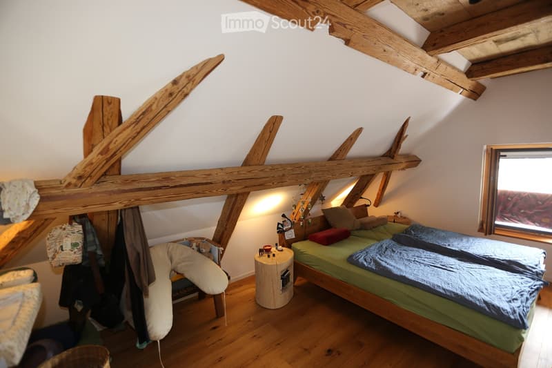 exposed wooden beams, double bed with blue sheets, small wooden side table, single bed, window, wooden floor