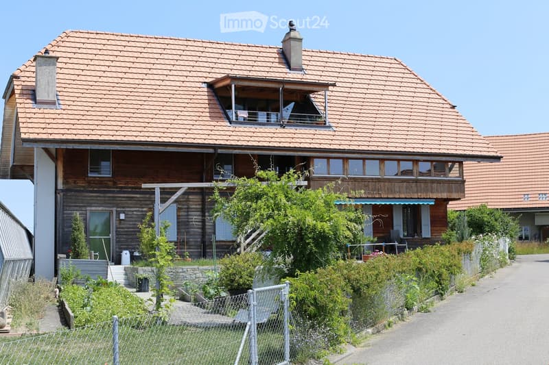 Wooden exterior, red roof, large windows, balcony, two chimneys, small garden, shrubs, gravel driveway