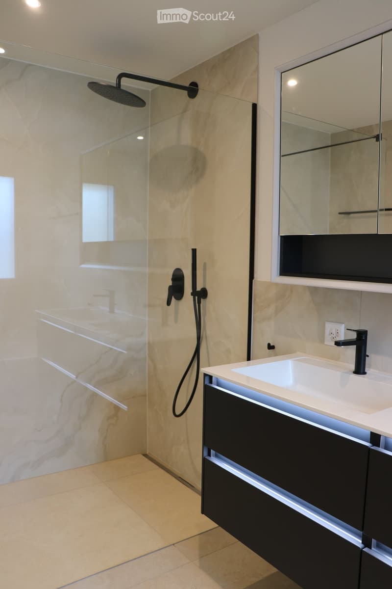 Marble walls, modern shower, white countertop, black cabinet, white sink, electrical outlet