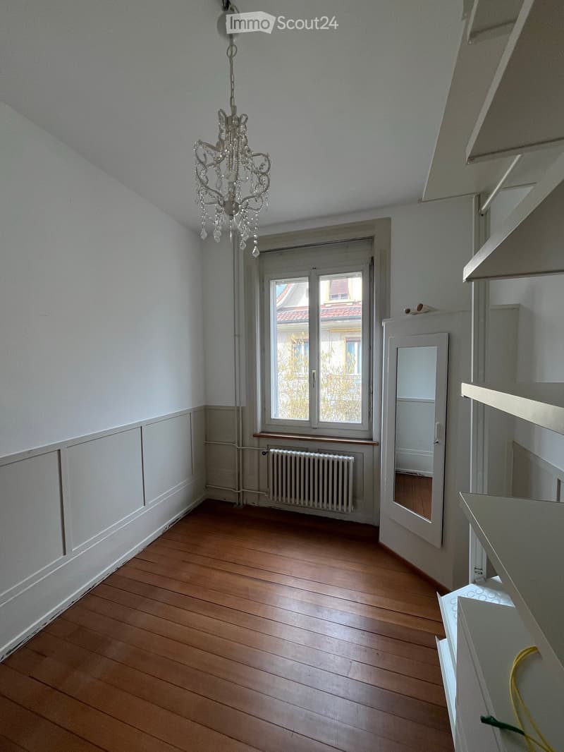 large room, wooden floor, white walls, large windows with radiators, crystal chandelier, large white door, mirror, white shelves