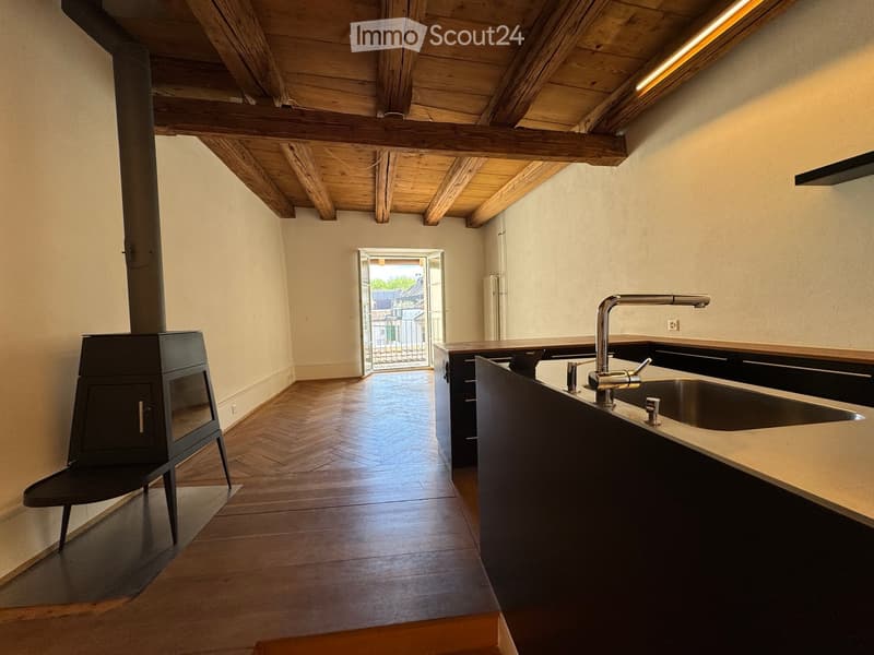Kitchen. Modern kitchen with wooden beams, wooden floor, and a sink with a modern faucet. A wooden chair is placed near a black stove.