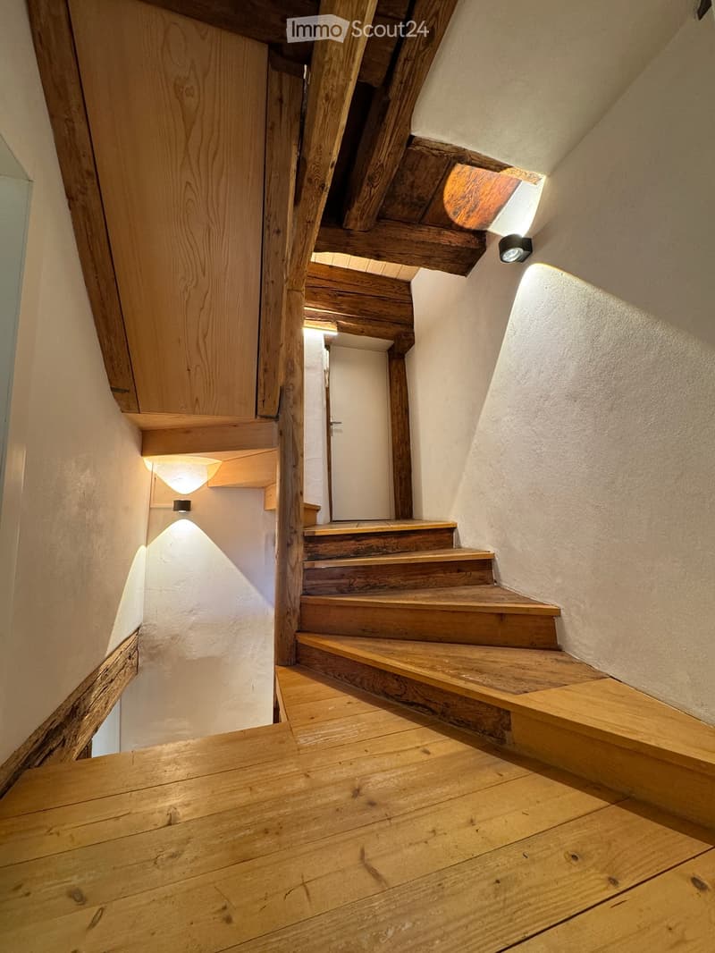 Corridor / Hallway. Wooden staircase with wooden railings and steps, illuminated by wall-mounted lights, leading to an open doorway.