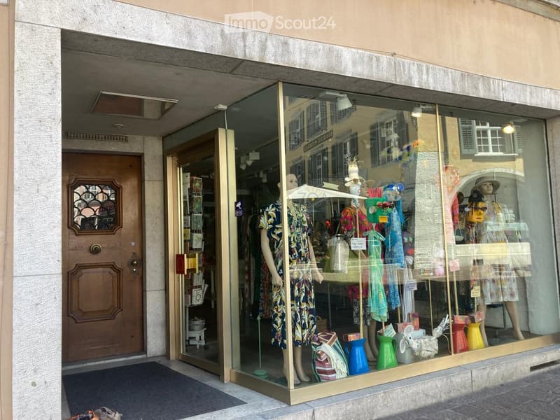A building with a glass storefront displaying mannequins and clothes, wooden door, and awning