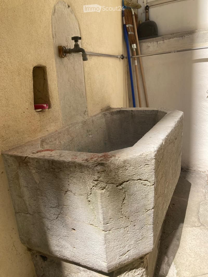 an old stone sink with a faucet, located in the corner of the room, next to a small hole, with some cleaning tools and brushes