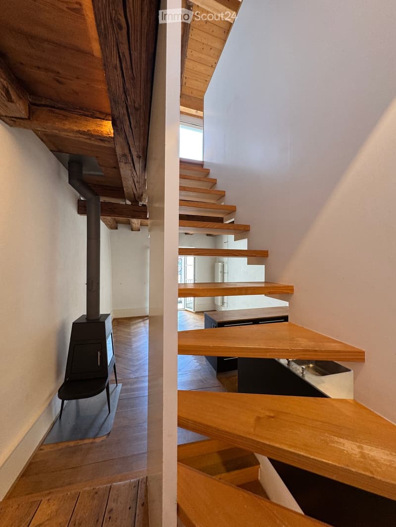 Corridor / Hallway. Modern wooden staircase with open wooden railings and a sleek black wood-burning stove in the adjacent room.