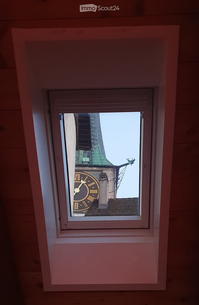 Ceiling window with wooden ceiling beams, church spire and clock tower visible through the window