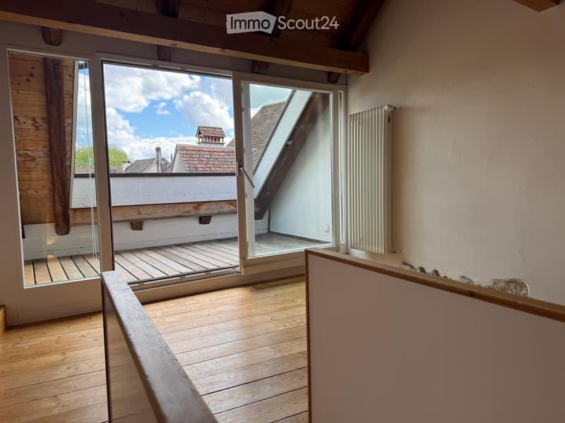 Unfurnished Room. Empty room with wooden flooring, large glass doors leading to a wooden deck, and a view of the roof and sky.