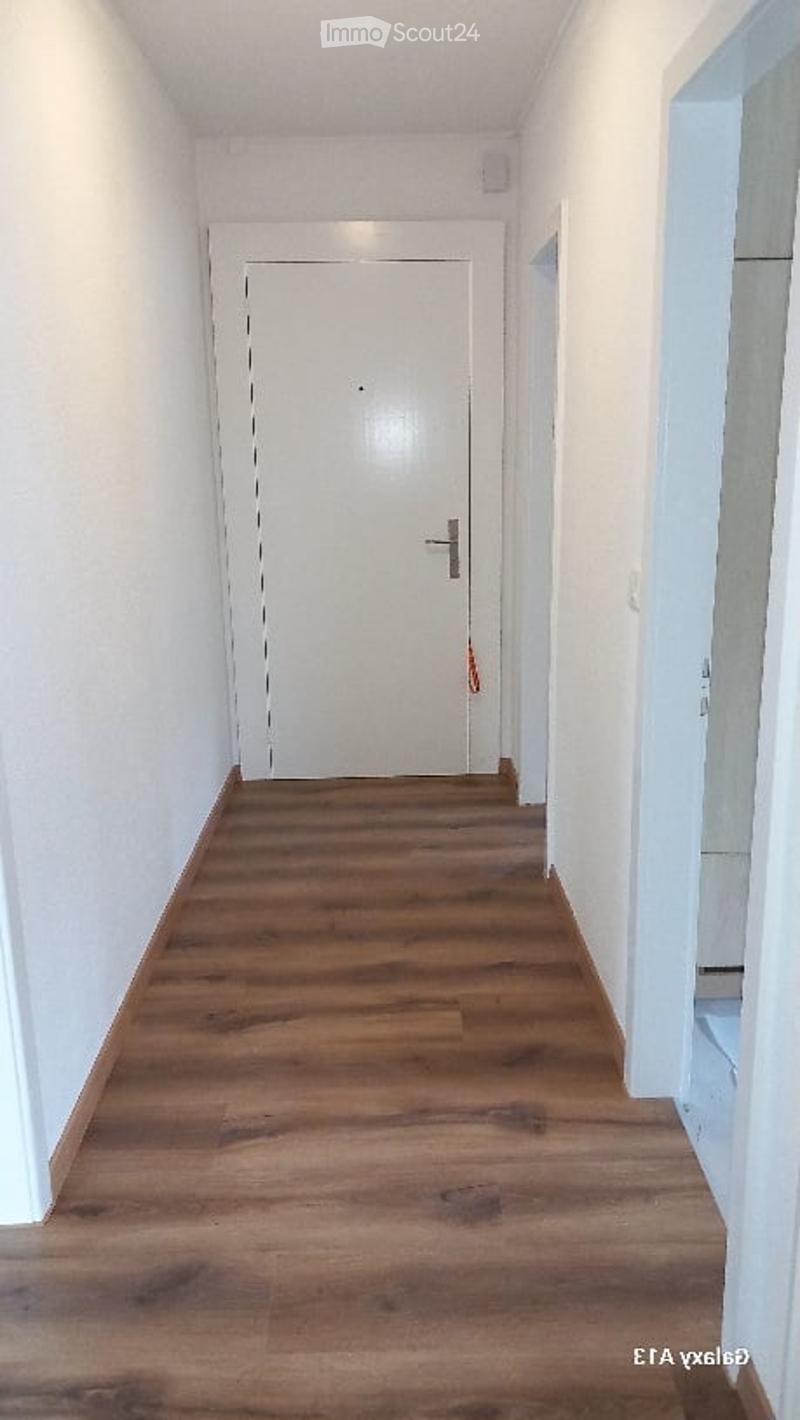 Empty corridor, wooden floor, white walls, closed door, small window, right side bathroom