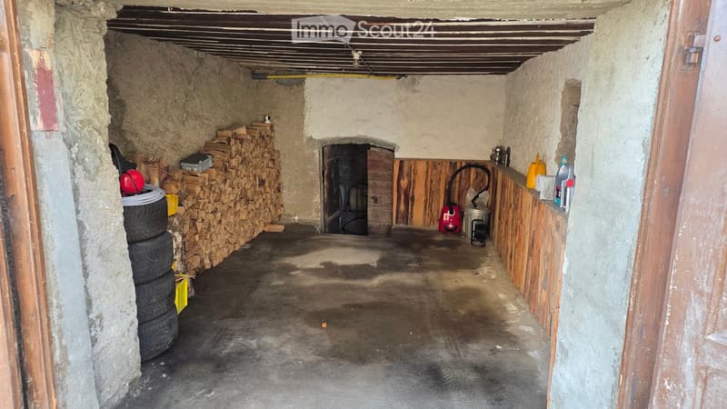 concrete walls, concrete floor, wood wall, stacks of firewood, tire, chimney, equipment and containers on wooden shelf