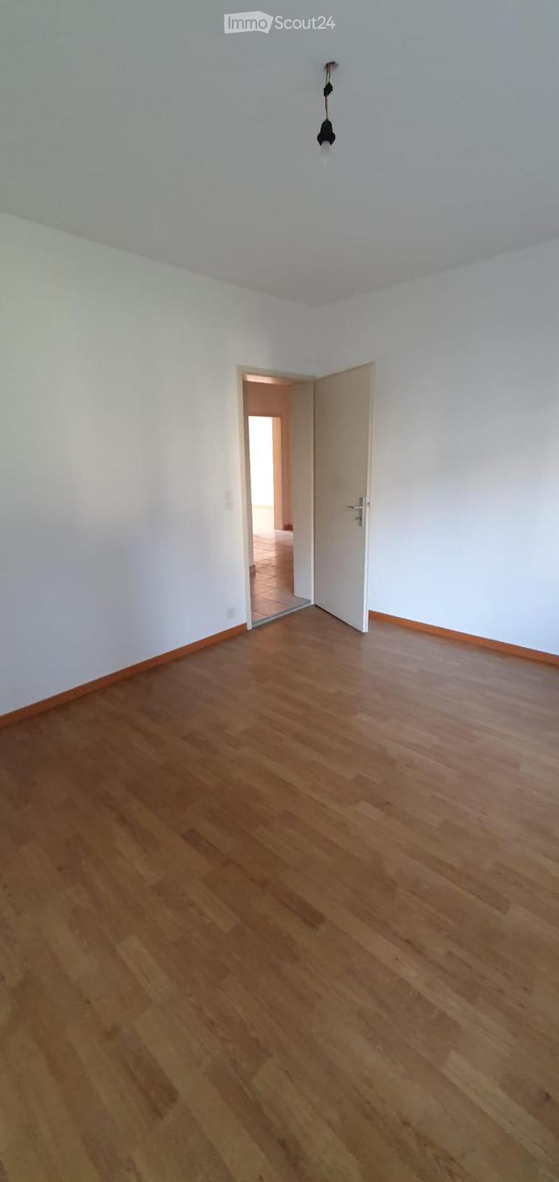 Empty room, wooden floor, white walls, open door leading to another room