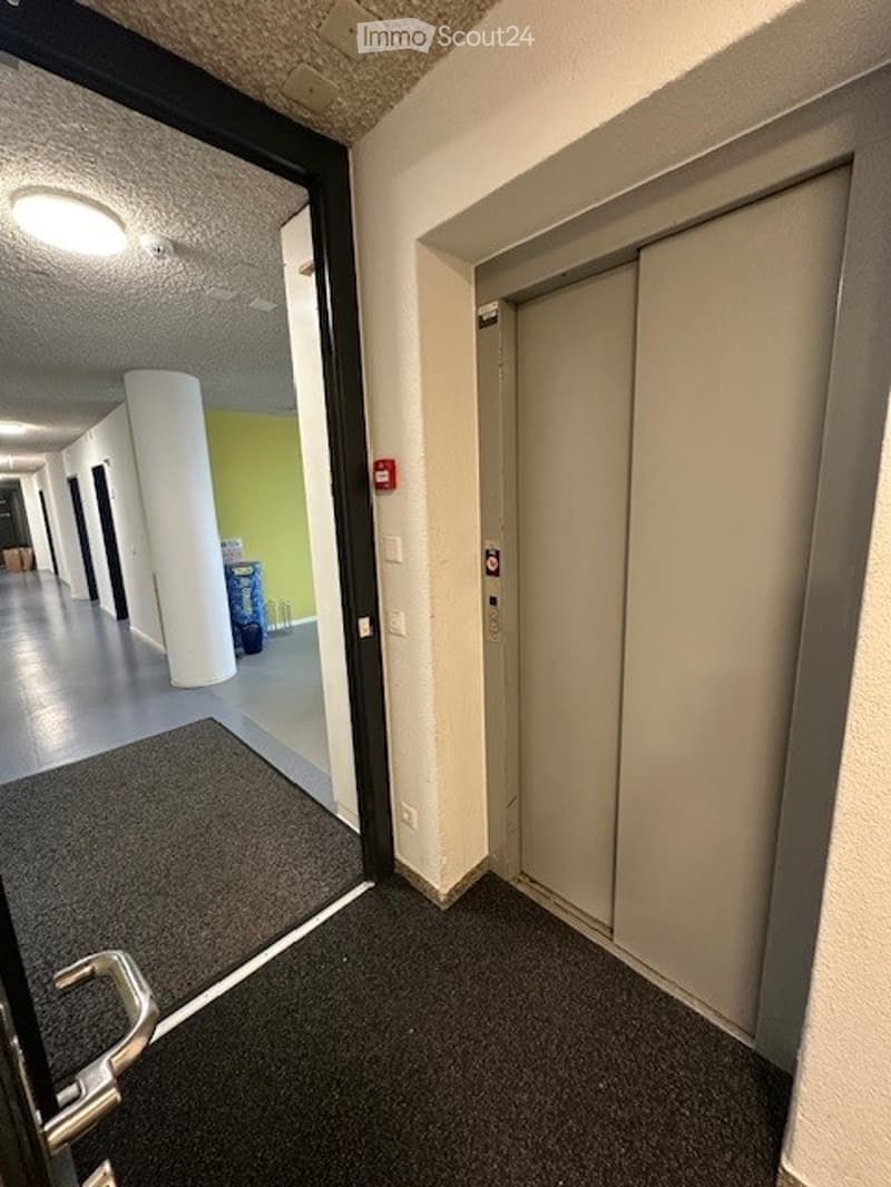 Elevator entrance with a carpeted floor, an open door, an elevator, a white pillar, a trash bin, and a ceiling light