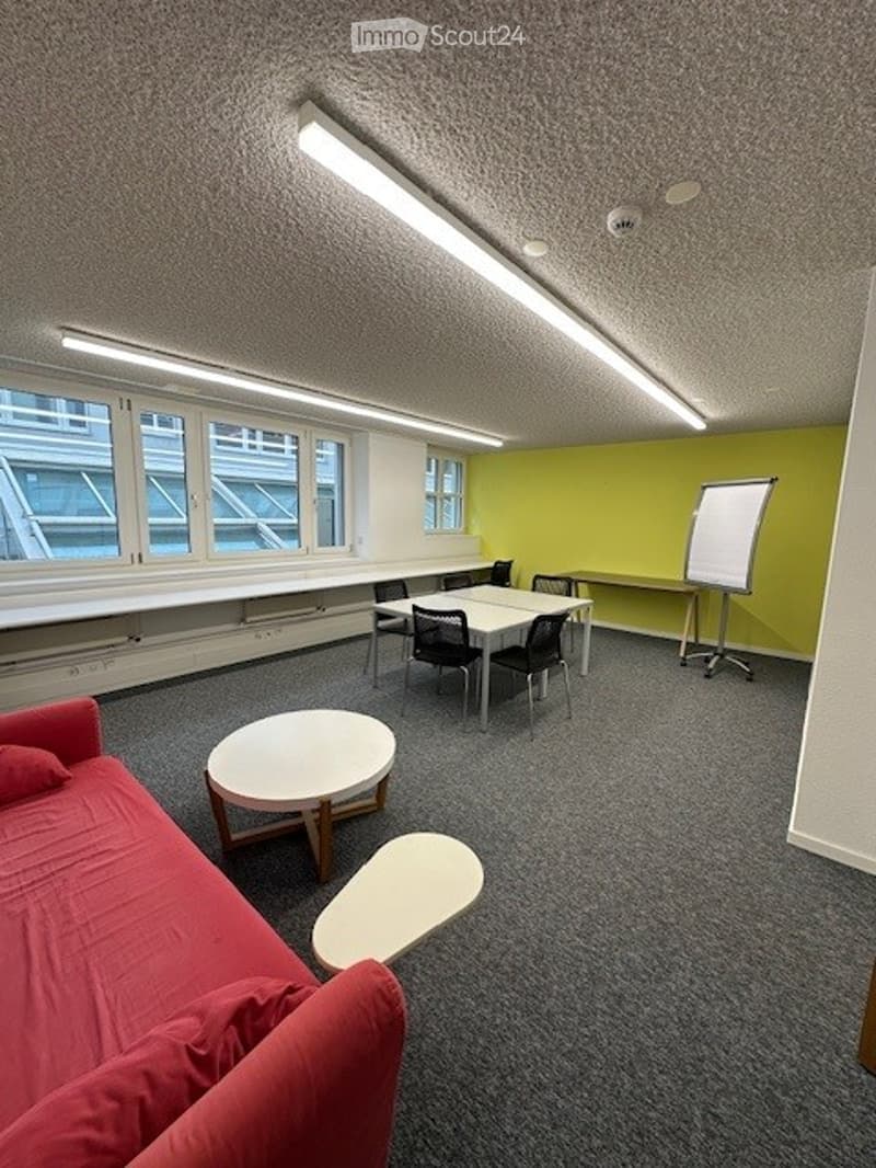 a vacant room with windows, carpet floor, tables, chairs, sofa, and a whiteboard