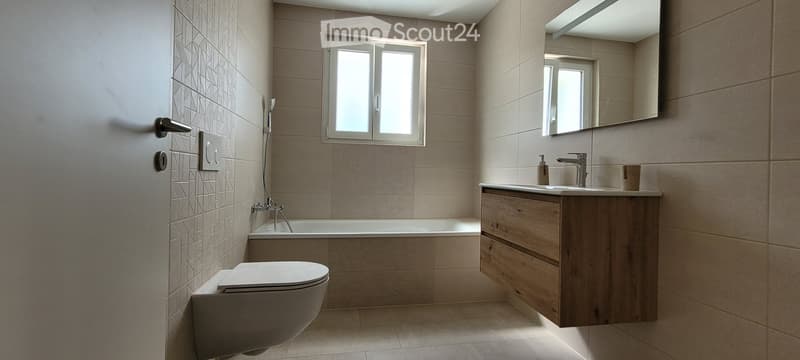 Modern bathroom with white tiles, bathtub, wooden vanity, and a mirror.