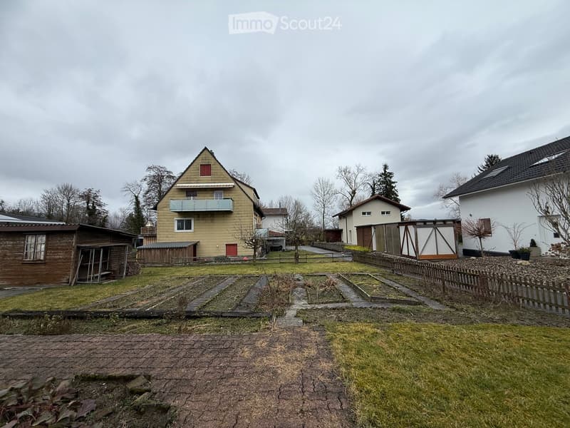 Garden with a variety of plants, trees, and shrubs, a walkway, a small building, and a fence
