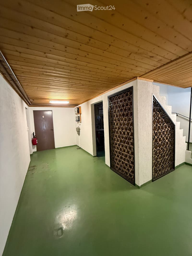 Garage room with green floor, wooden ceiling, wall mounted fire extinguisher and open door