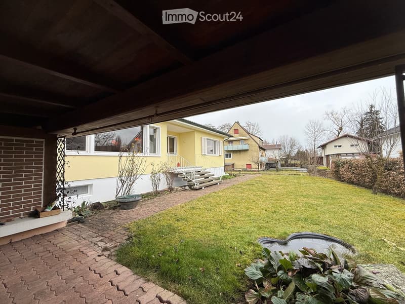 covered patio, brick flooring, fenced yard, lawn, small pond, plants, and shrubs