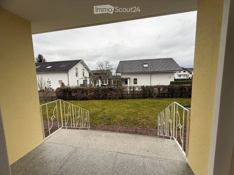 covered balcony with white railings, looking out onto a manicured garden with green grass