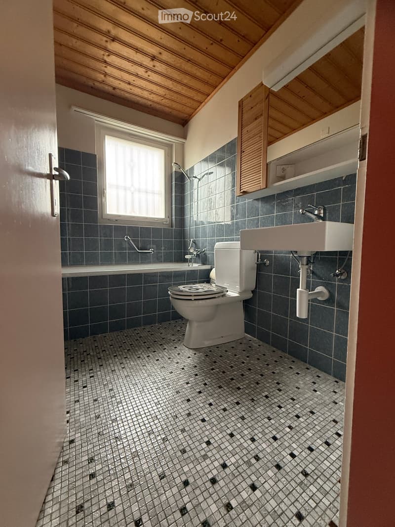 Small bathroom with bathtub, shower head, toilet, sink, and blue tiled walls and floor.