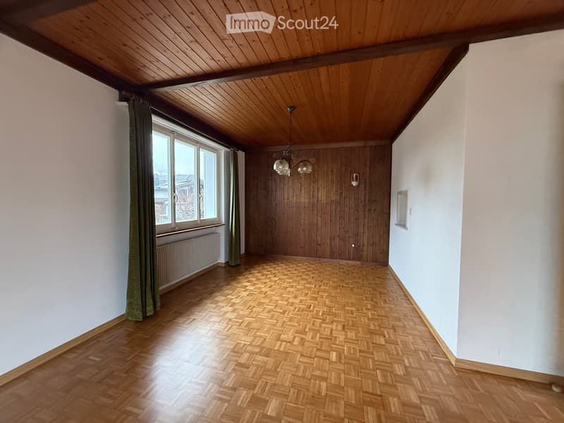 Empty room, parquet flooring, wooden beams ceiling, white walls, large window, radiator, ceiling lamp.