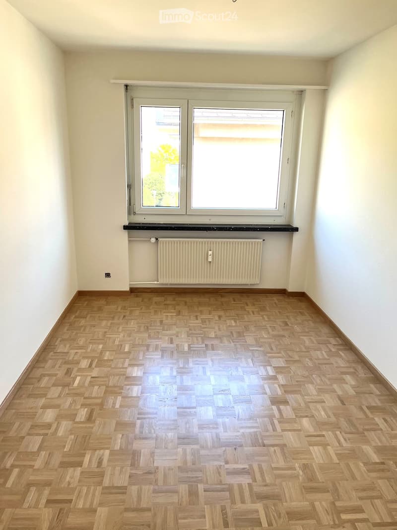 spacious room with parquet floor, large window with wooden frame, white walls, white radiator below window