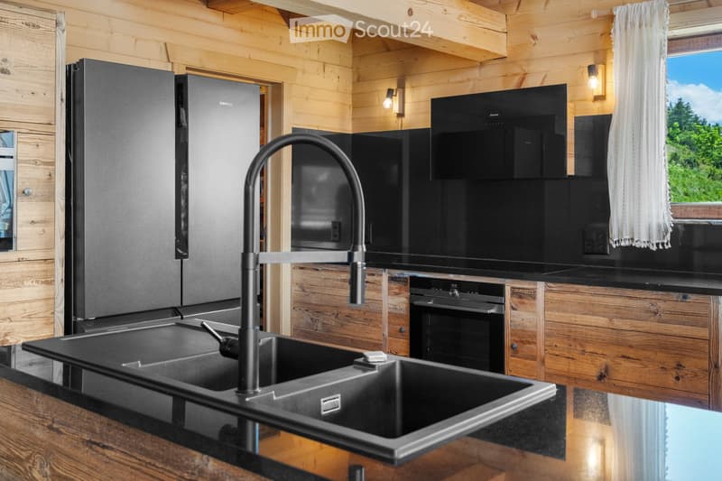 Modern kitchen with black appliances, including a refrigerator and dishwasher, built into a wooden cabinet and wall paneling. The kitchen features a black sink with a black faucet and a wooden countertop.