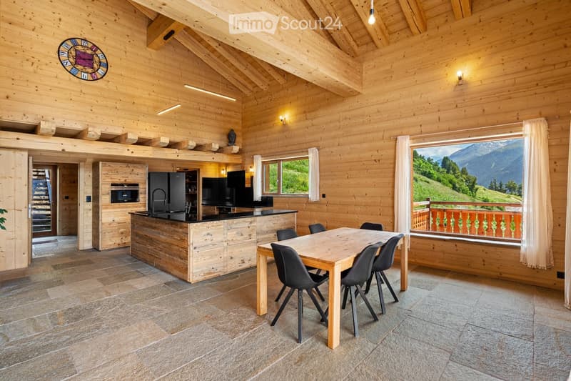 Spacious open-plan living area with wooden walls and ceiling, large windows offering a scenic mountain view, a modern kitchen with a central island, and a dining table with chairs.