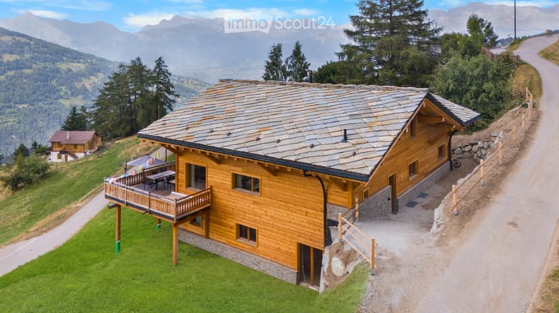 Two story house with balcony, wooden exterior, slate roof, nestled in the mountains