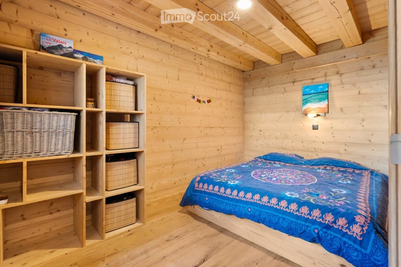 Cozy wooden bedroom with built-in shelves, a blue patterned bedspread, and a framed artwork on the wall