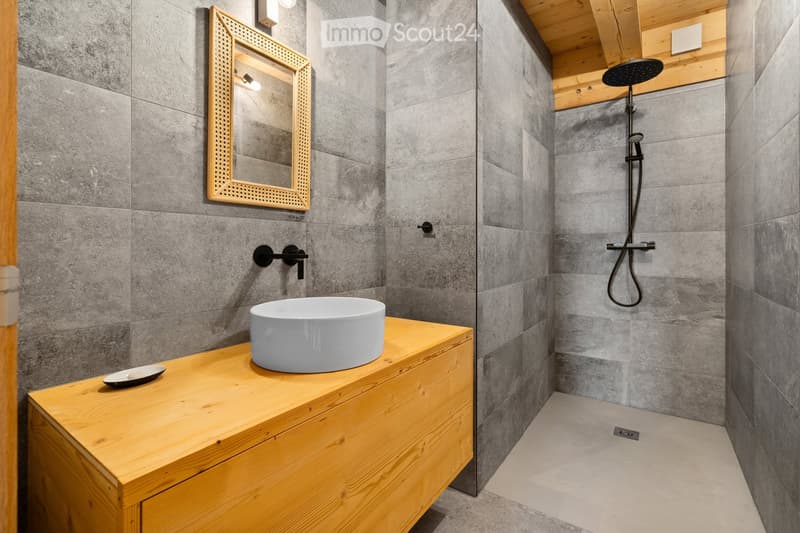 Modern bathroom with gray tile walls, wooden vanity with a white vessel sink, and a rainfall shower head