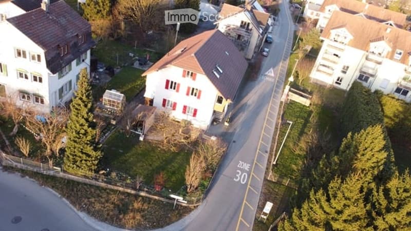 Aerial view of the building, located on the corner of the street, surrounded by other houses, and green grass, white windows