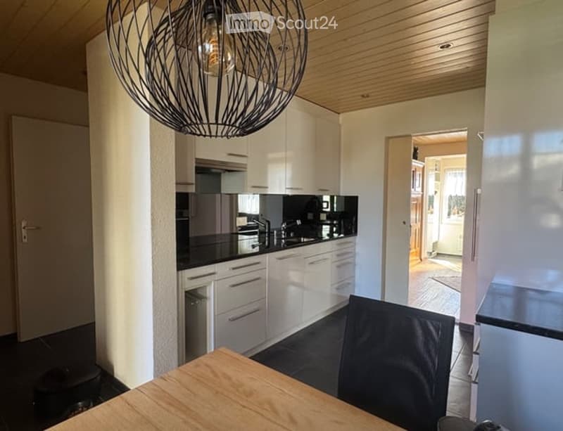 White cabinets, black countertops, hanging lamp, stainless steel sink, faucet, black chair, wooden table