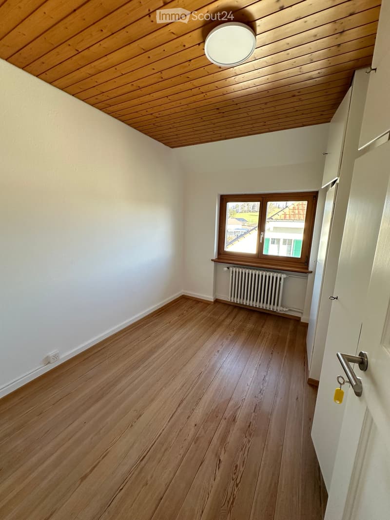 wooden floor, white walls, radiator, round ceiling light, window