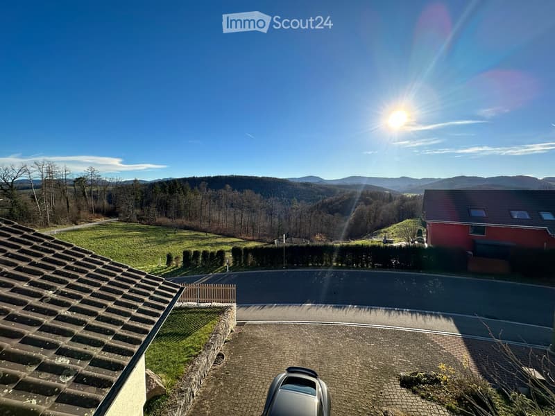 Mountain landscape, driveway with car, greenery, sunlight, and hills in the distance
