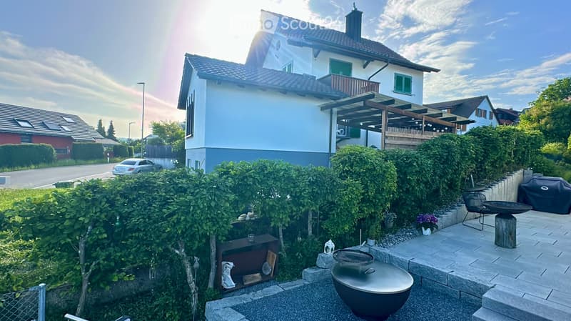 Well-maintained garden with a patio area, barbecue, outdoor furniture, and a modern house in the background.