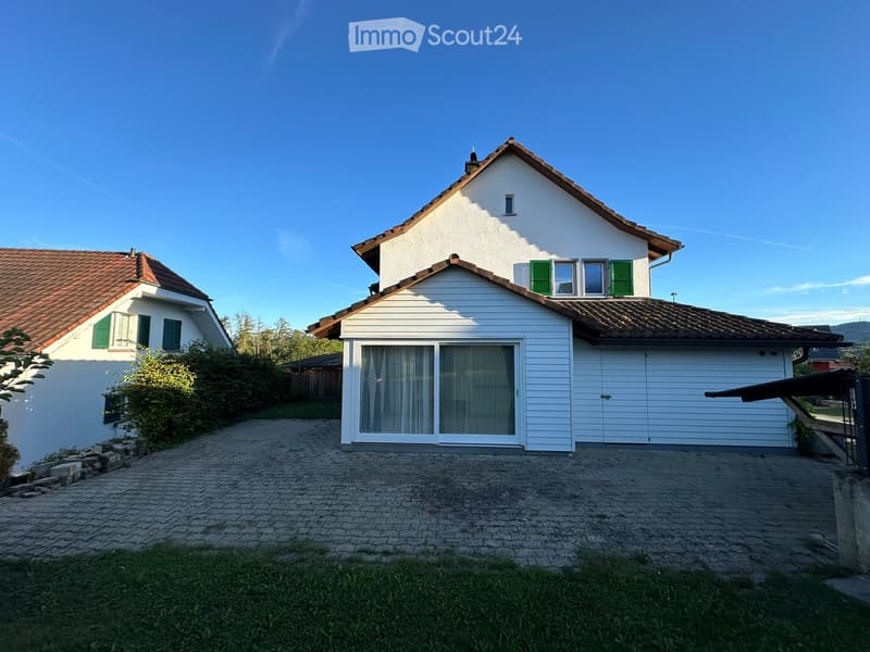 Two-story white house with red-tiled roof, green shutters, large garage, and driveway.