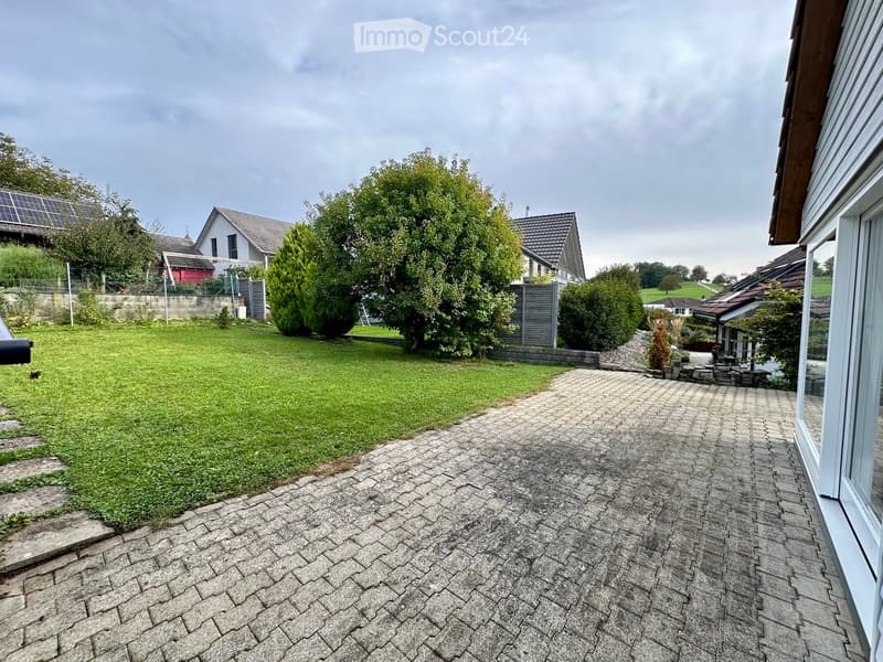 Well-maintained garden with a paved pathway leading to a house, surrounded by greenery and neighboring houses.