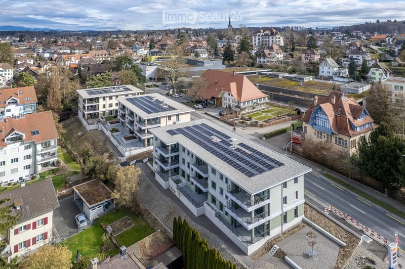 Multiple residential buildings, solar panels on rooftops, parking lot, street with traffic