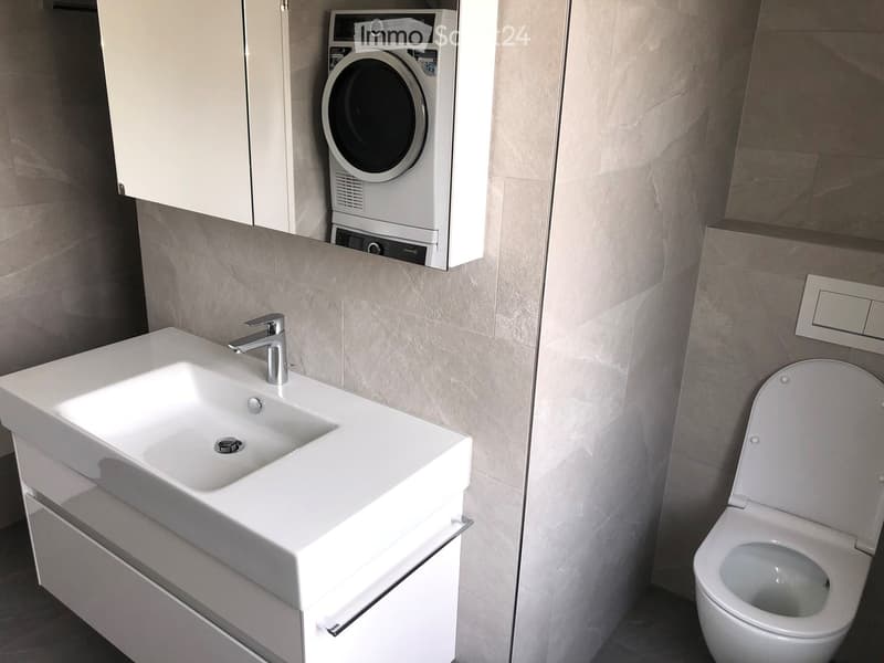white tiled wall, white tiled floor, white vanity with sink, toilet and washing machine mounted on wall