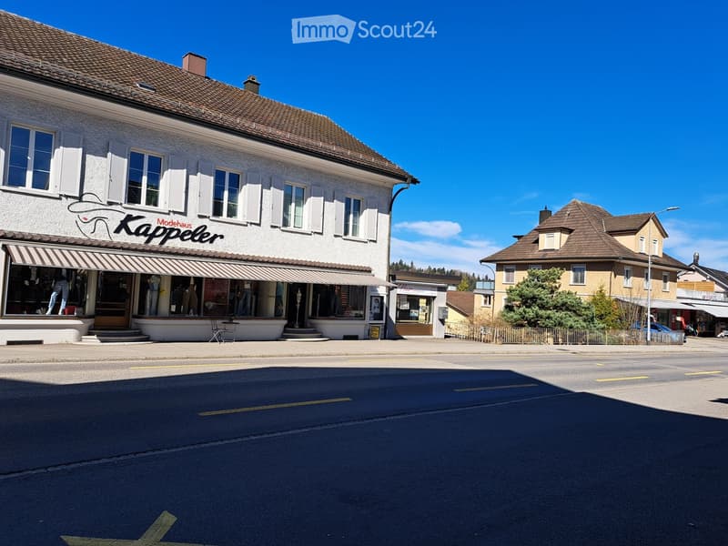 two story commercial building, storefronts with awnings, street with a car parked on the side, another house in the background, sunny weather