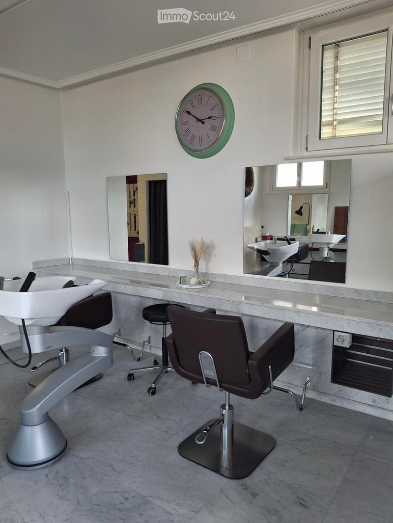 Barber shop: white countertop, 2 white sinks, 2 salon chairs, 1 stool, white and gray wall, clock