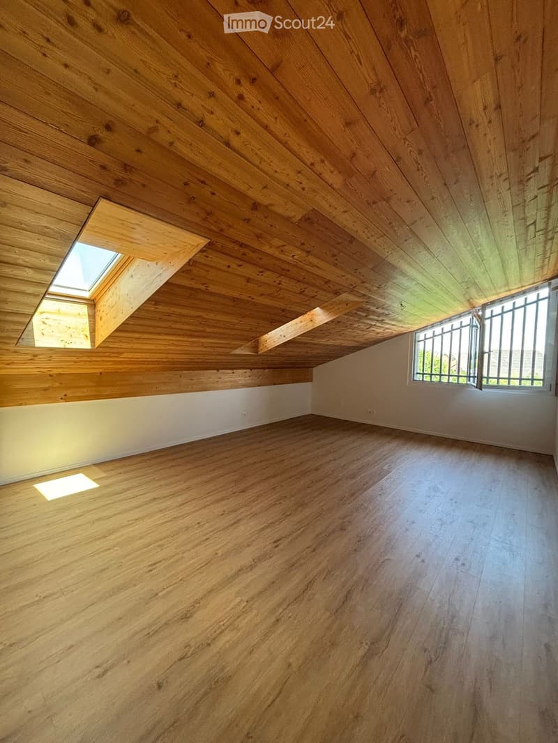 Empty room with wooden floors and walls, featuring a skylight and a window with bars.