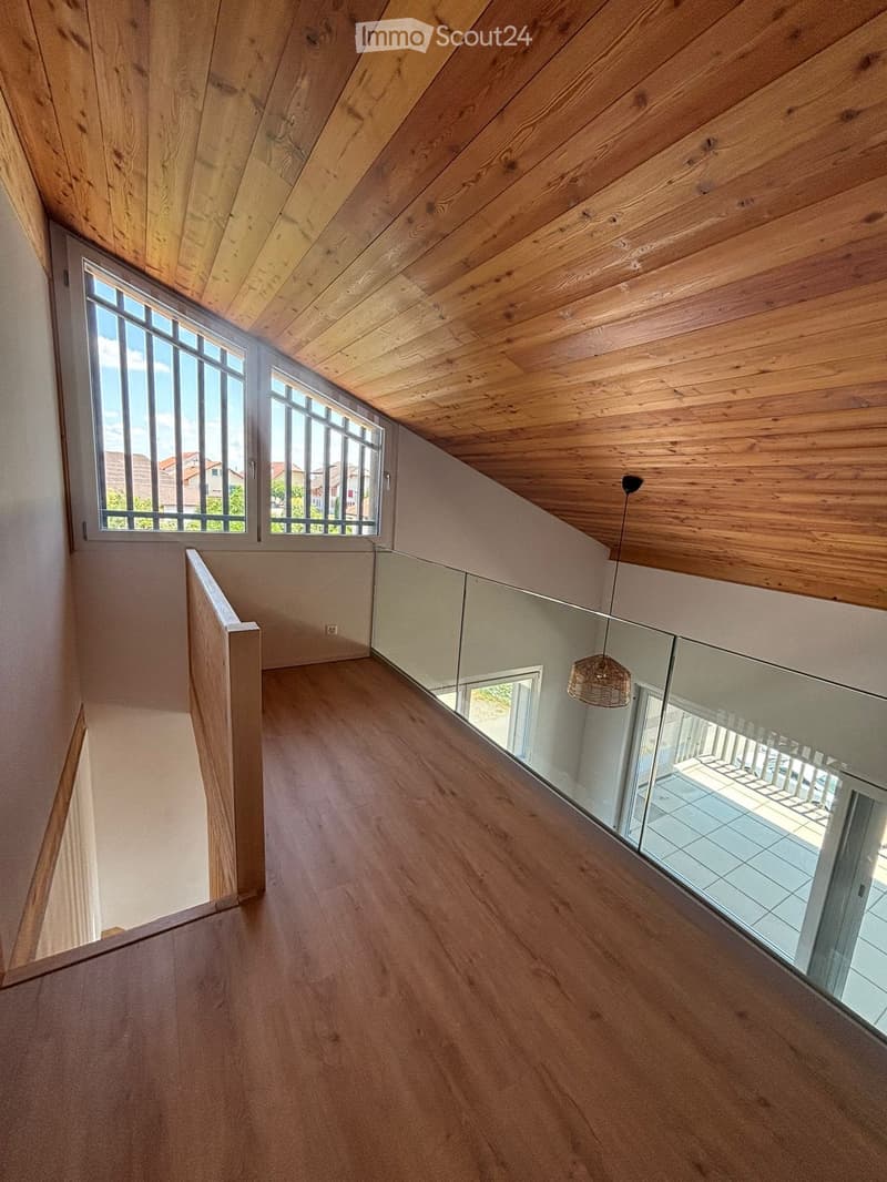 Spacious hallway with wooden flooring and ceiling, large windows, glass railing leading to a balcony area.