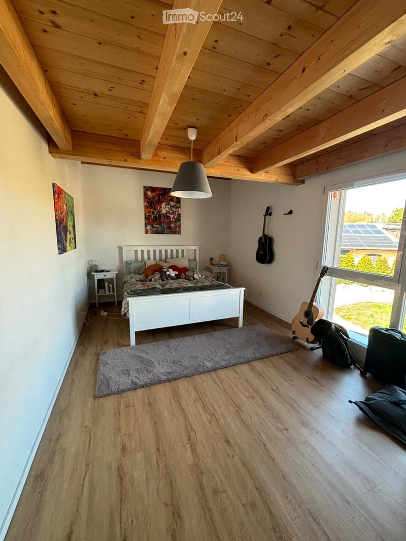 Bedroom with wooden floor, white walls, wooden ceiling, bed, rug, guitars, paintings, nightstands, lamps