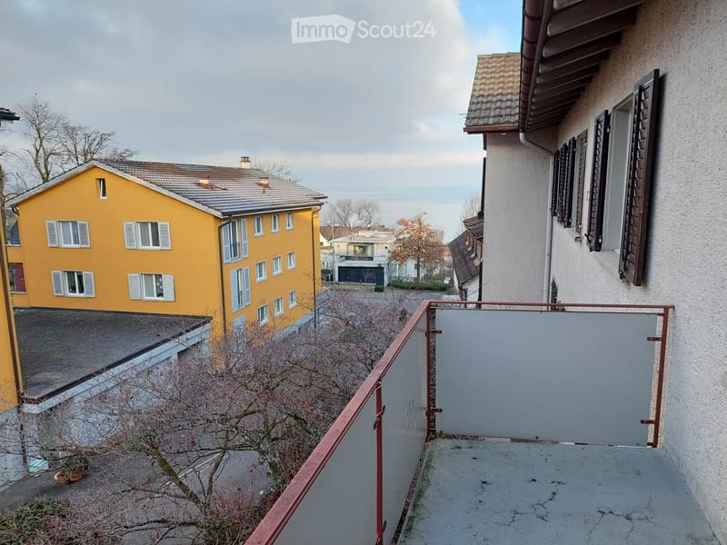 2 story house with yellow walls, large balcony with glass railings, tree in front, view of the road and trees