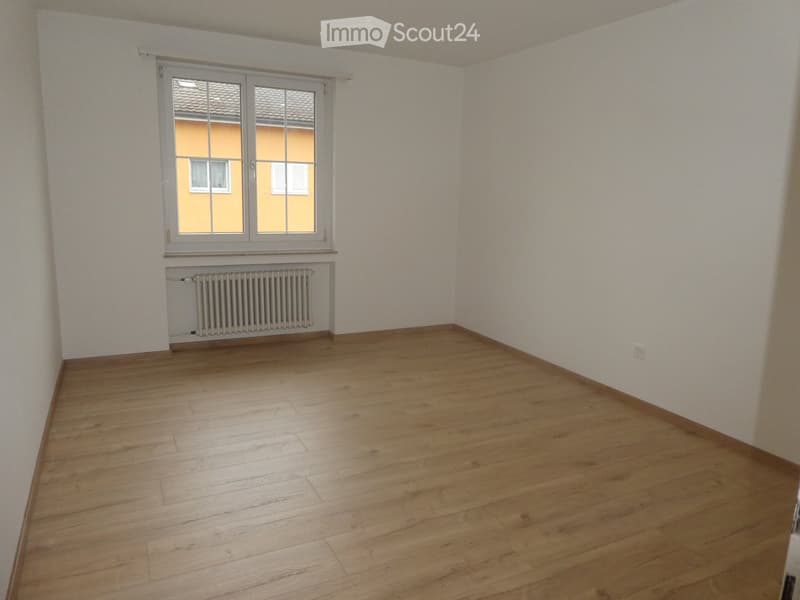 empty room, white walls, wooden floor, large window, white radiator, power outlet