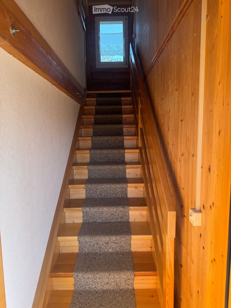 Wooden stairs leading to a door, wooden handrail, white wall