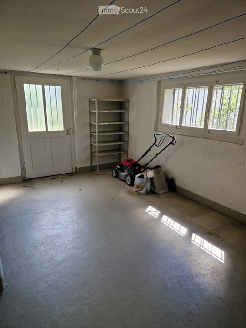 Empty garage with doors, windows, storage shelf, and a lawnmower on the floor.
