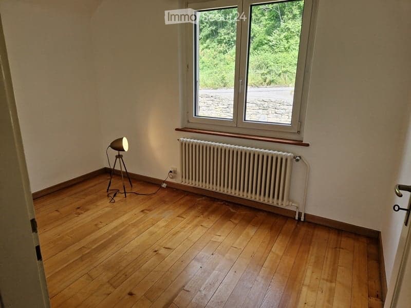 empty room with wooden floor, white walls, white radiator, white window, table lamp, electrical outlet