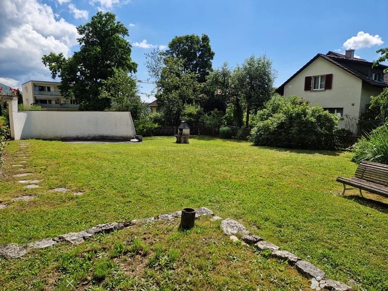 green lawn with concrete path, white wall, bench, fireplace, trees