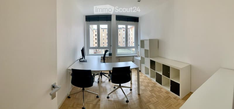 A room with two desks, chairs, computer monitor, and storage units.
